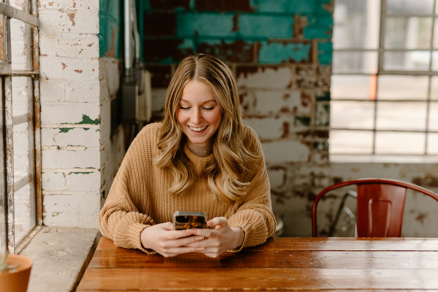 A person sitting in a café, smiling as they look something up on their phone